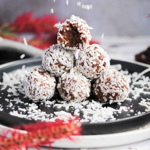 stack of coconut covered energy balls with bite taken out of top and coconut flakes falling down