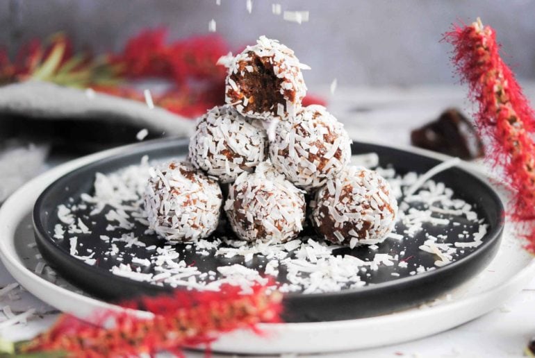 stack of coconut covered energy balls with bite taken out of top and coconut flakes falling down