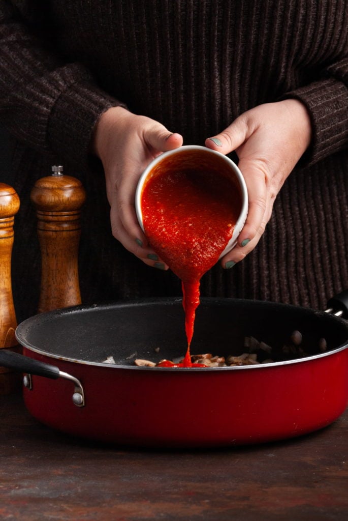 adding marinara sauce to a hot pan with cooked mushrooms and onions