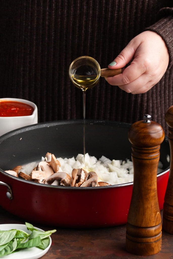 adding olive oil to pan with mushrooms and onions in a pan