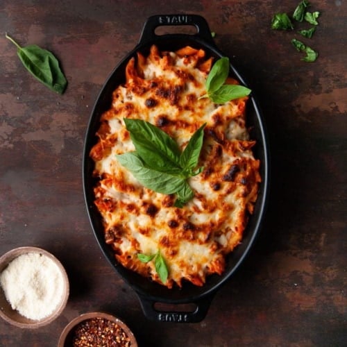 Easy Cheesy Pasta Bake in a black oval baking dish garnished with basil