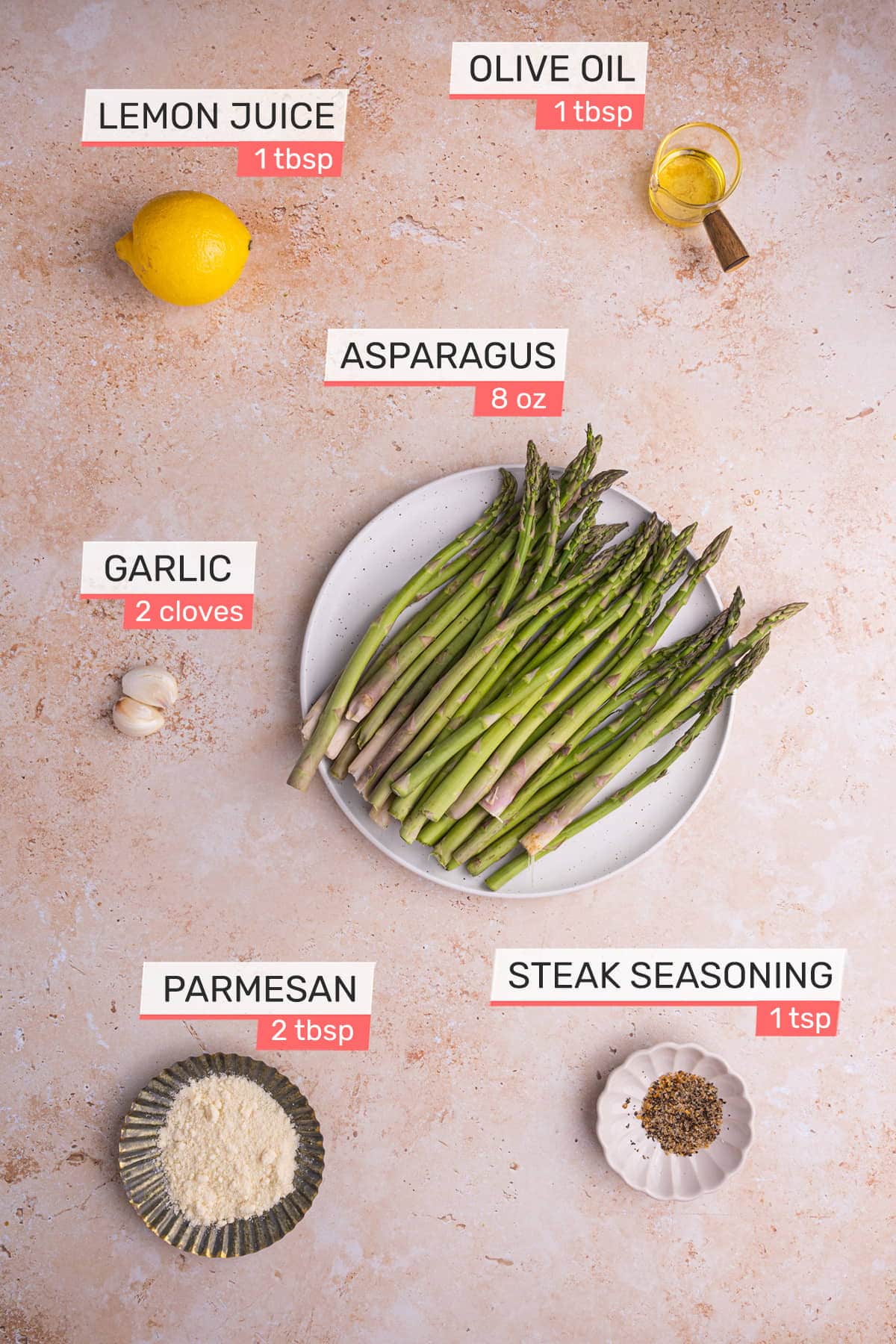 overhead view of all ingredients needed for garlic lemon asparagus on a pink granite background - asparagus, olive oil, lemon, garlic, parmesan, steak seasoning