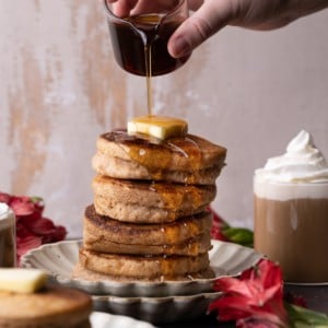pouring maple syrup onto tall stack of pancakes