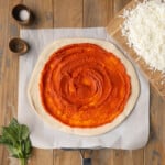 Fresh tomato pizza sauce spread on top of raw pizza dough.