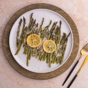 Overhead shot of Garlic Lemon Asparagus on a white plate with two slices of lemon on top