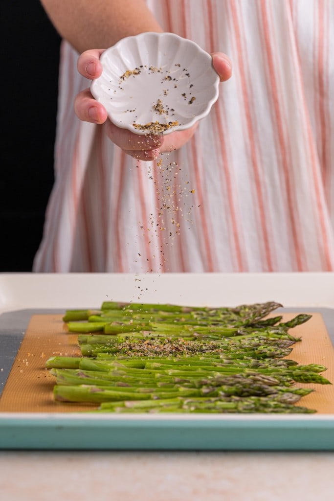adding steak seasoning to asparagus