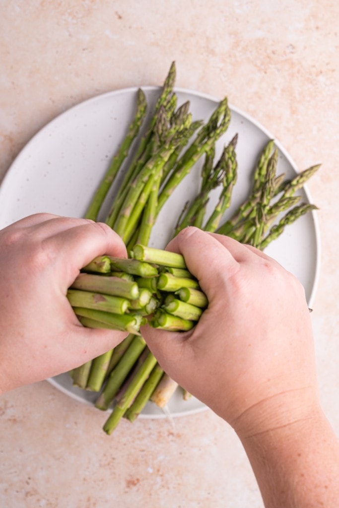 using two hands to snap asparagus at woody ends