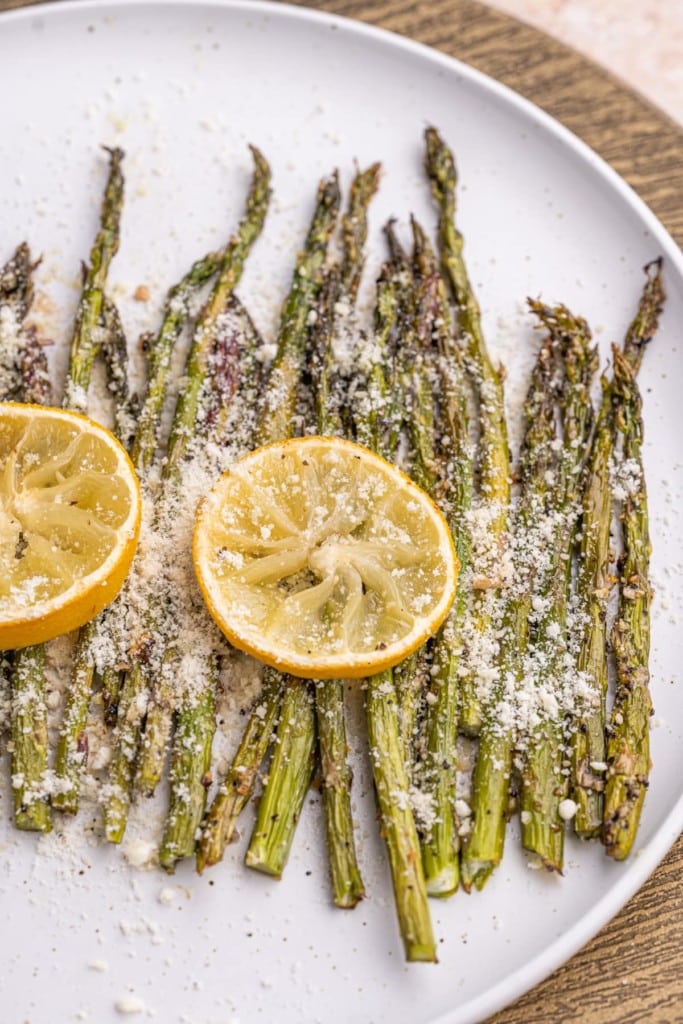 Close up of Garlic Lemon Asparagus on a white plate with two slices of lemon on top