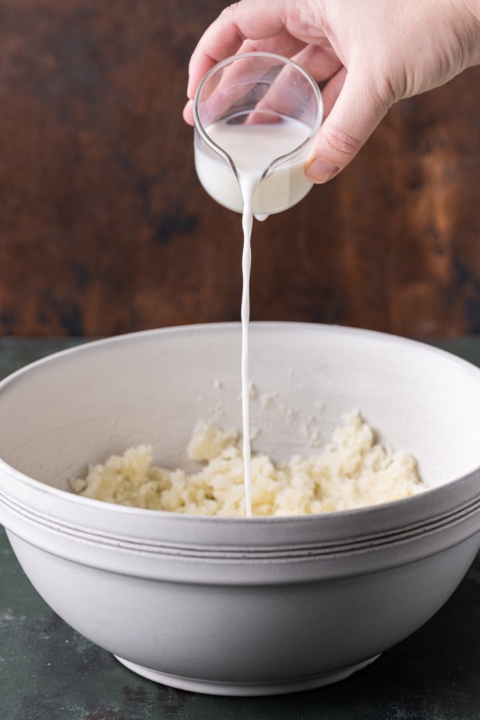 Slowly adding milk to mashed potatoes, stirring in between to get the right consistency