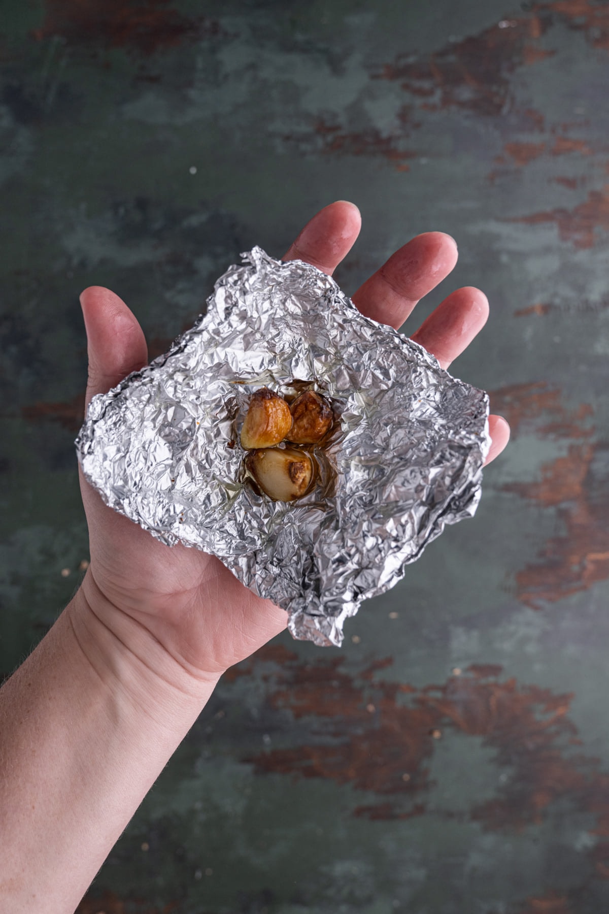 Holding aluminum foil with 3 whole cloves of roasted garlic