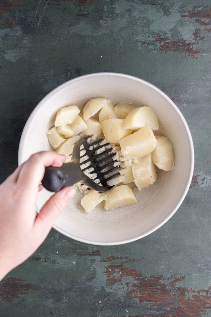 Using a potato masher to finely mash boiled Russett potatoes