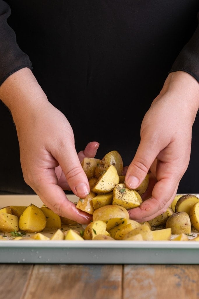 using clean hands to toss potato chunks in olive oil