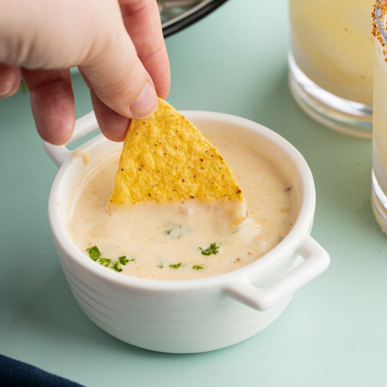 dipping a chip into a small pot of Queso Blanco