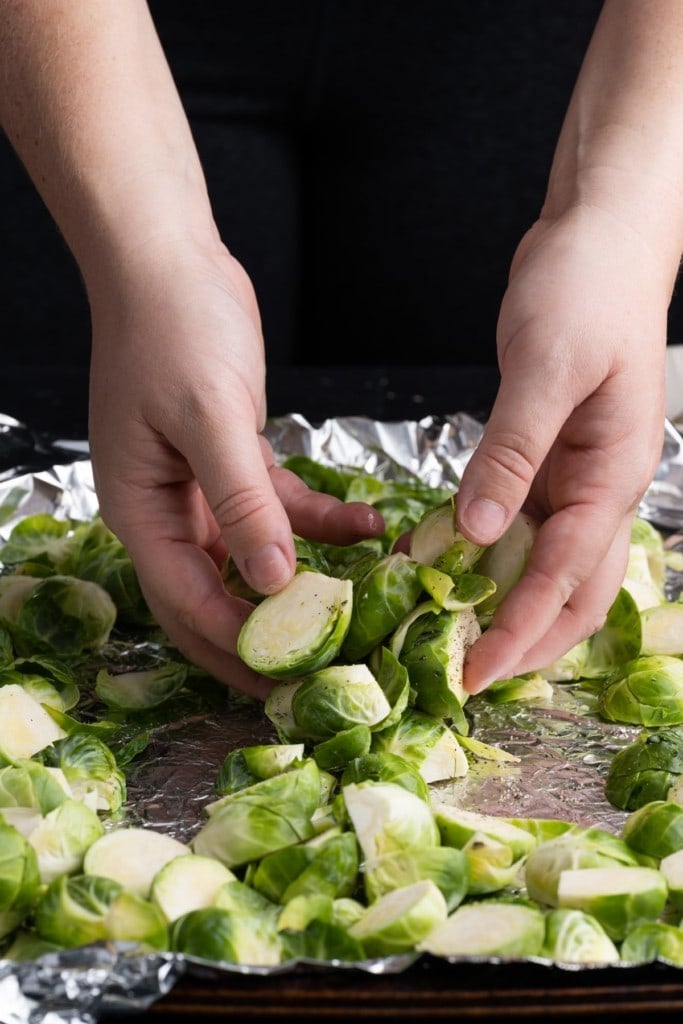 using clean hands to toss brussels sprouts to ensure they are evenly coated in oil and seasoning