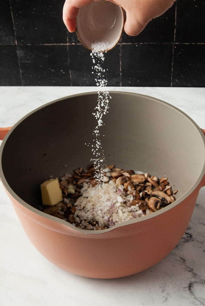 seasoning mushrooms and shallots with salt in a big pot