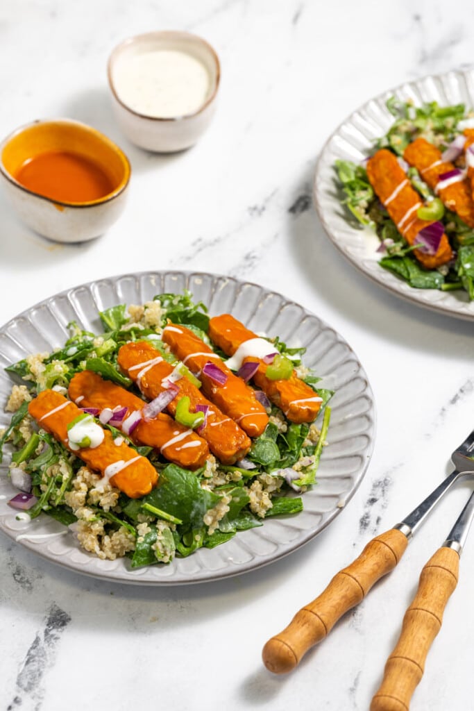 Two plates of quinoa and greens with buffalo tofu