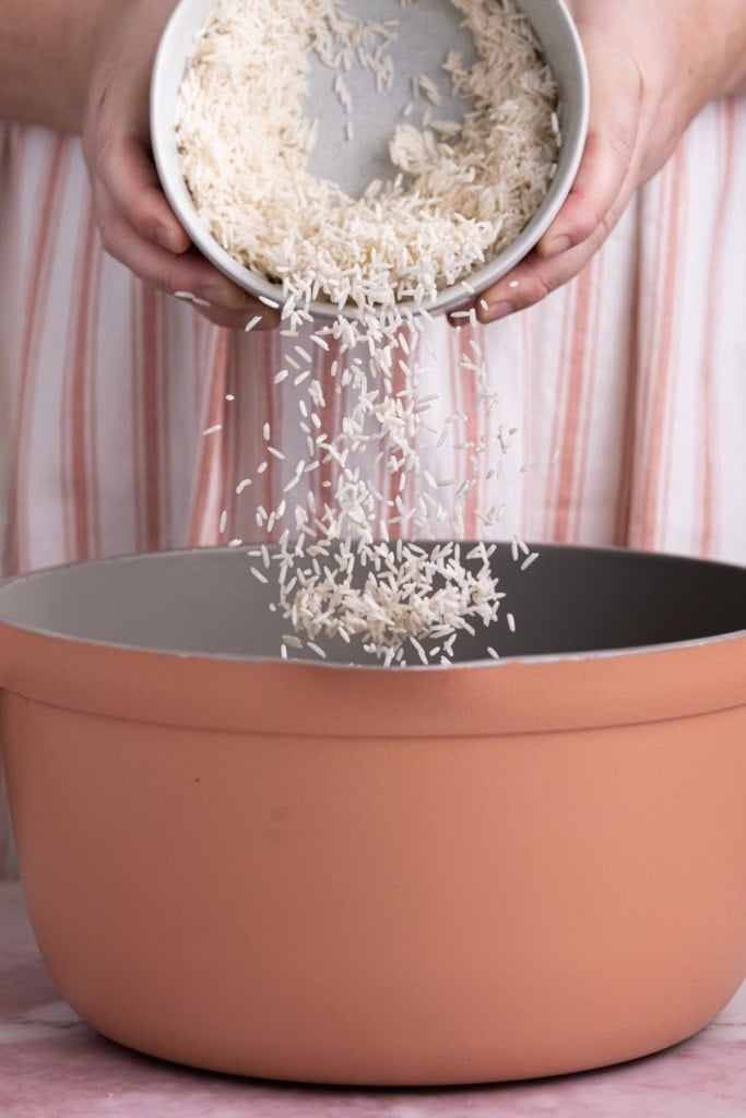 Pouring Basmati rice into large pot with vegetable broth and saffron