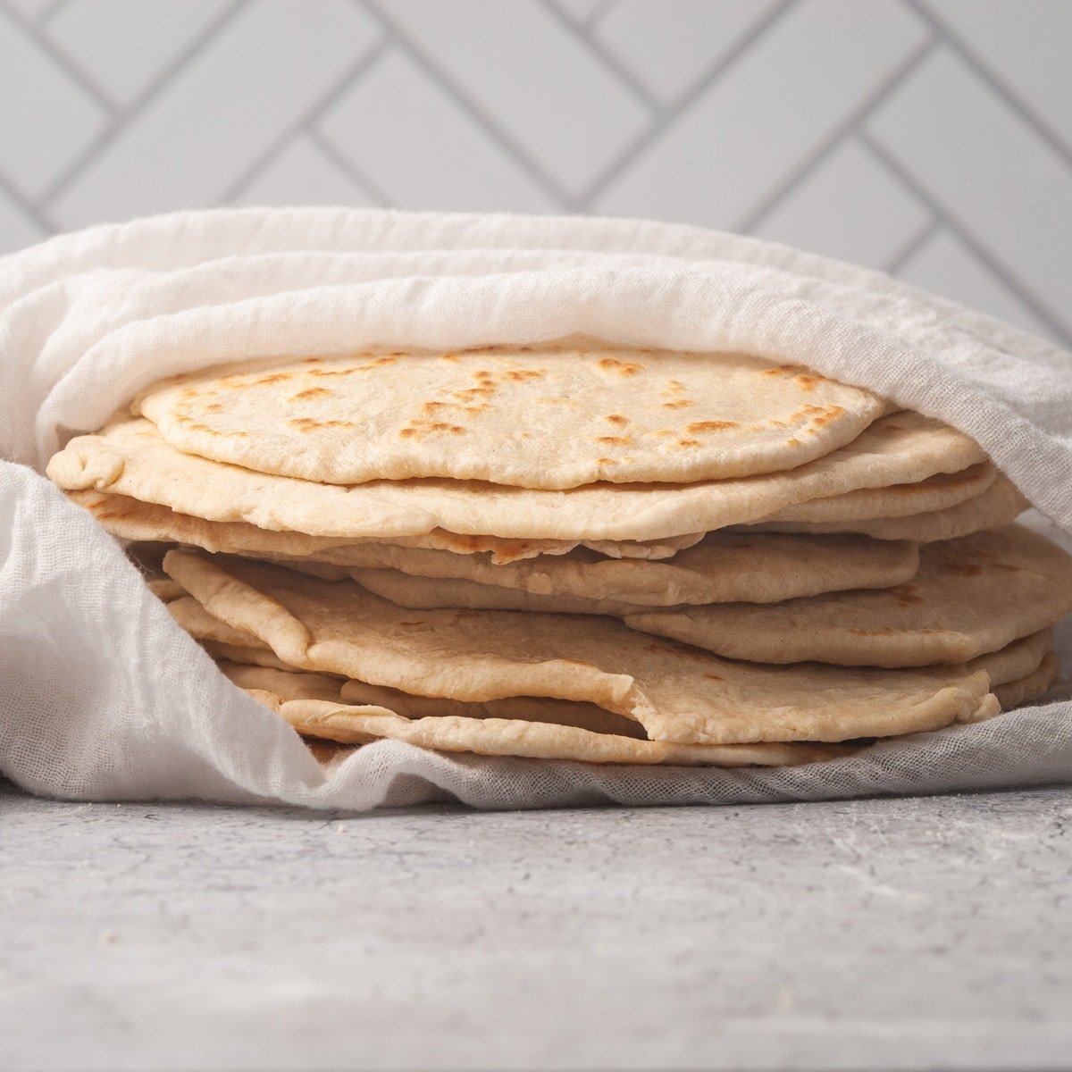stack of homemade fluffy flour tortillas wrapped in a kitchen towel