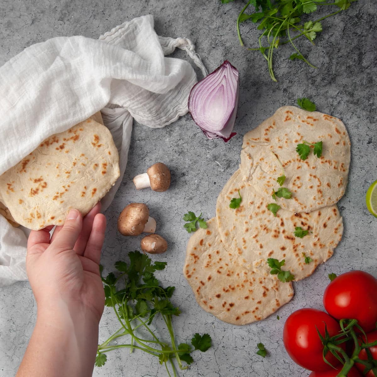 hand grabbing a tortilla from the pile to stuff it with fresh ingredients