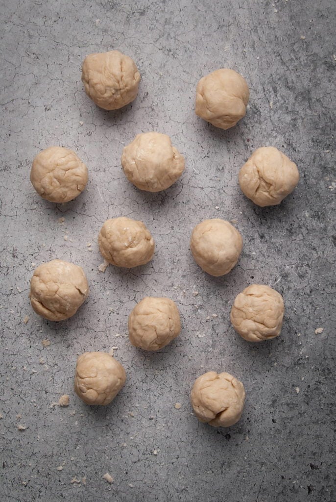 12 balls of flour tortilla dough lined up next to one another. 