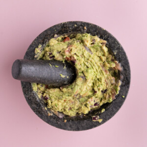 Smashed avocado, red onion, and tomato in a mortar with salt