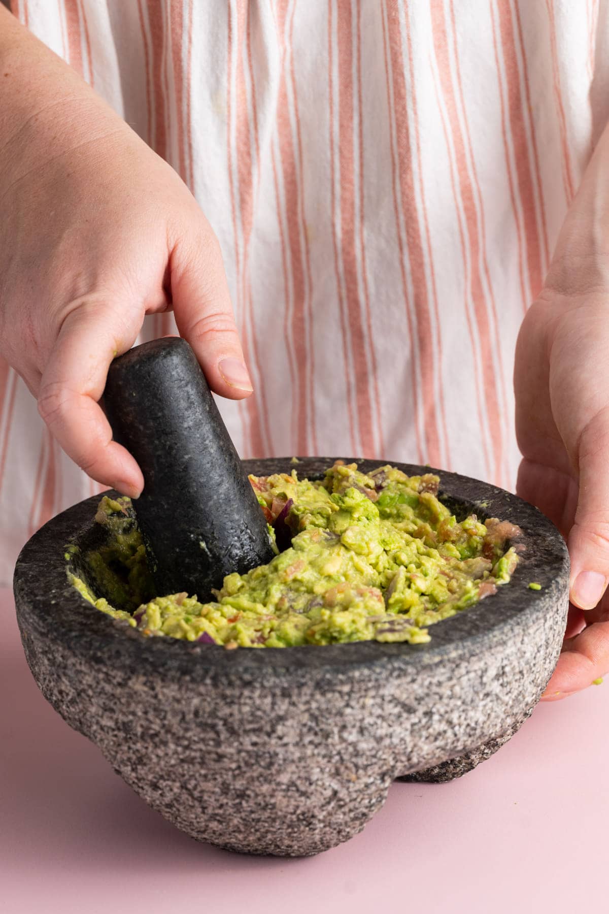 Using pestle to crush avocado with red onion and tomato