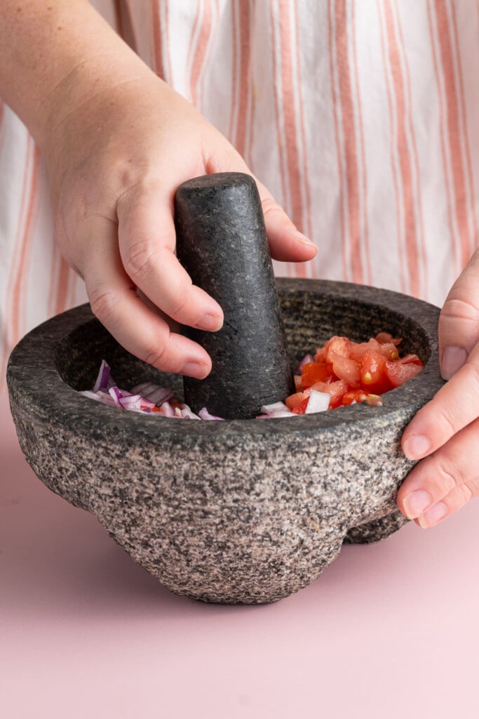 Crushing red onion and tomatoes in mortar with a pestle