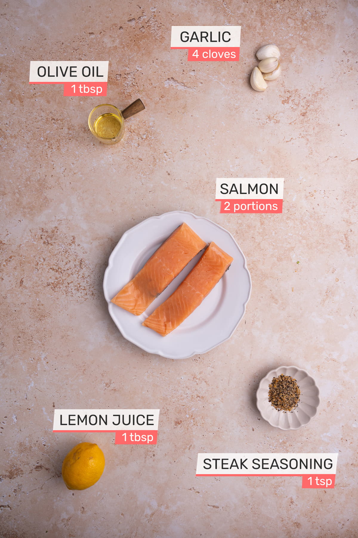 overhead view of all ingredients needed for roasted garlic salmon on a pink granite background - salmon, olive oil, lemon, garlic, steak seasoning