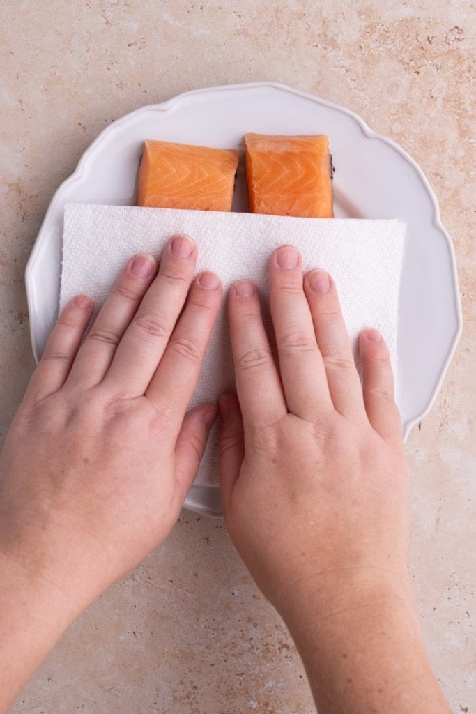 Using a paper towel to pat dry excess moisture off of salmon fillets