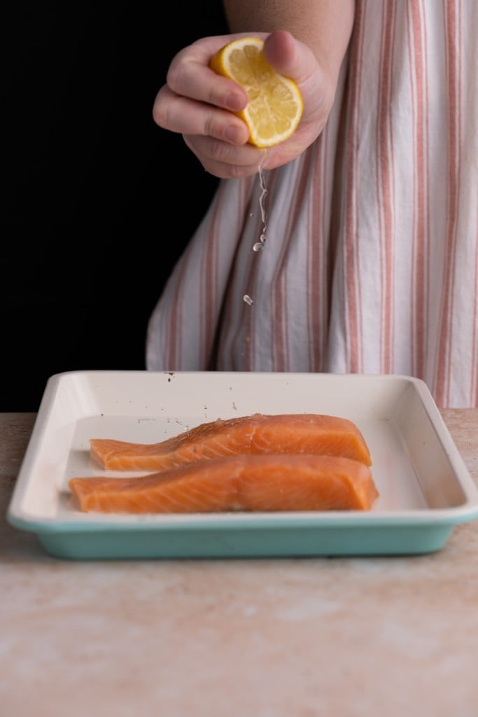 squeezing lemon juice onto salmon fillets