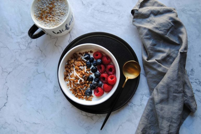 Overhead picture of a bowl of granola with berries and yoghurt, alongside a cup of coffee