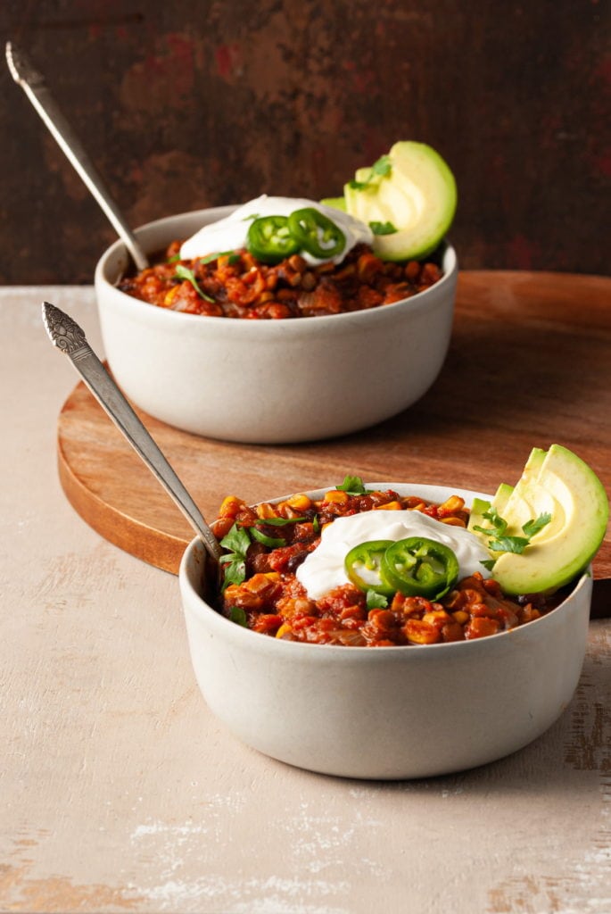 two bowls of vegan chili with lentils with silver spoons in each