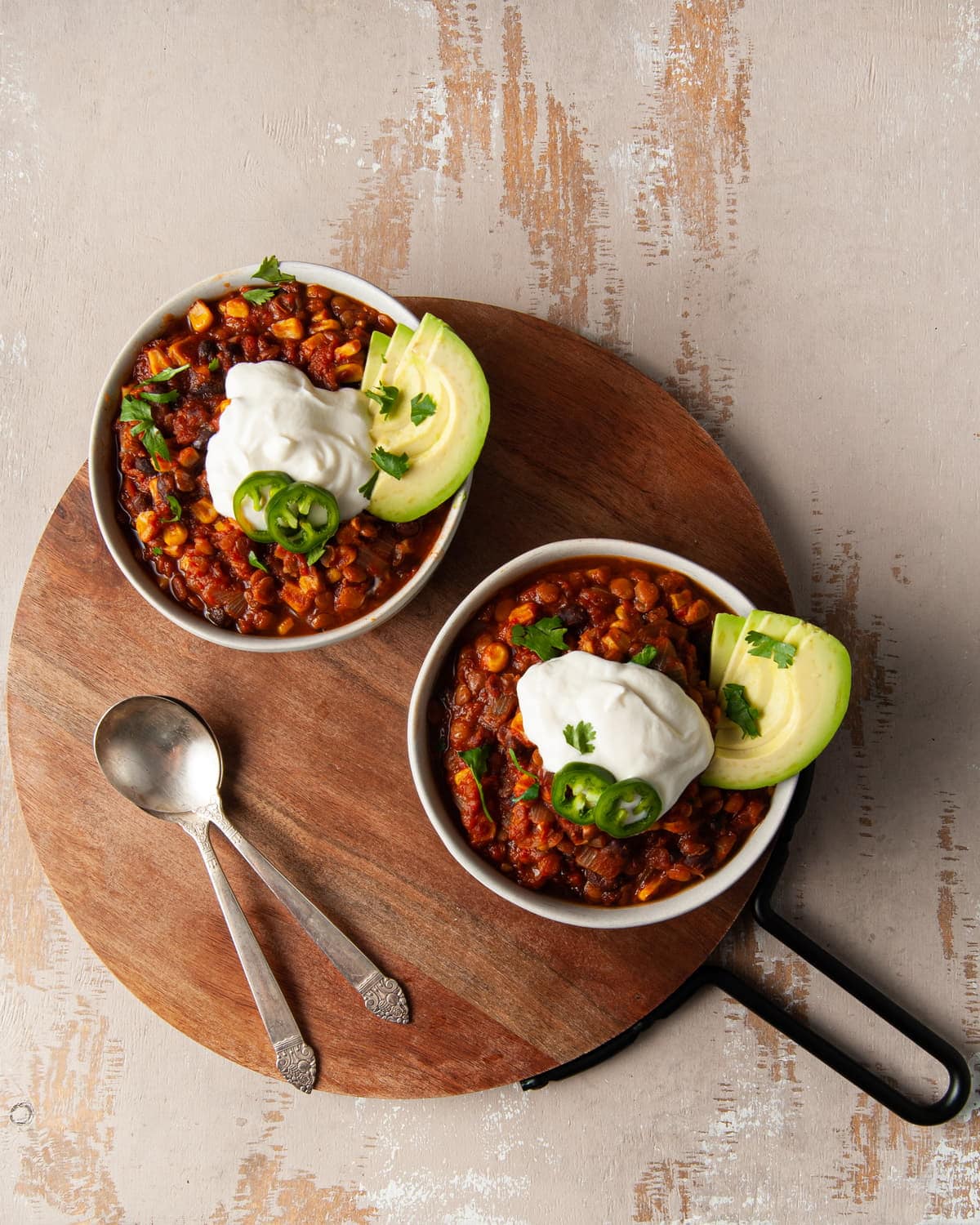 overhead shot of two bowls of vegan chili with lentils on a round wooden board