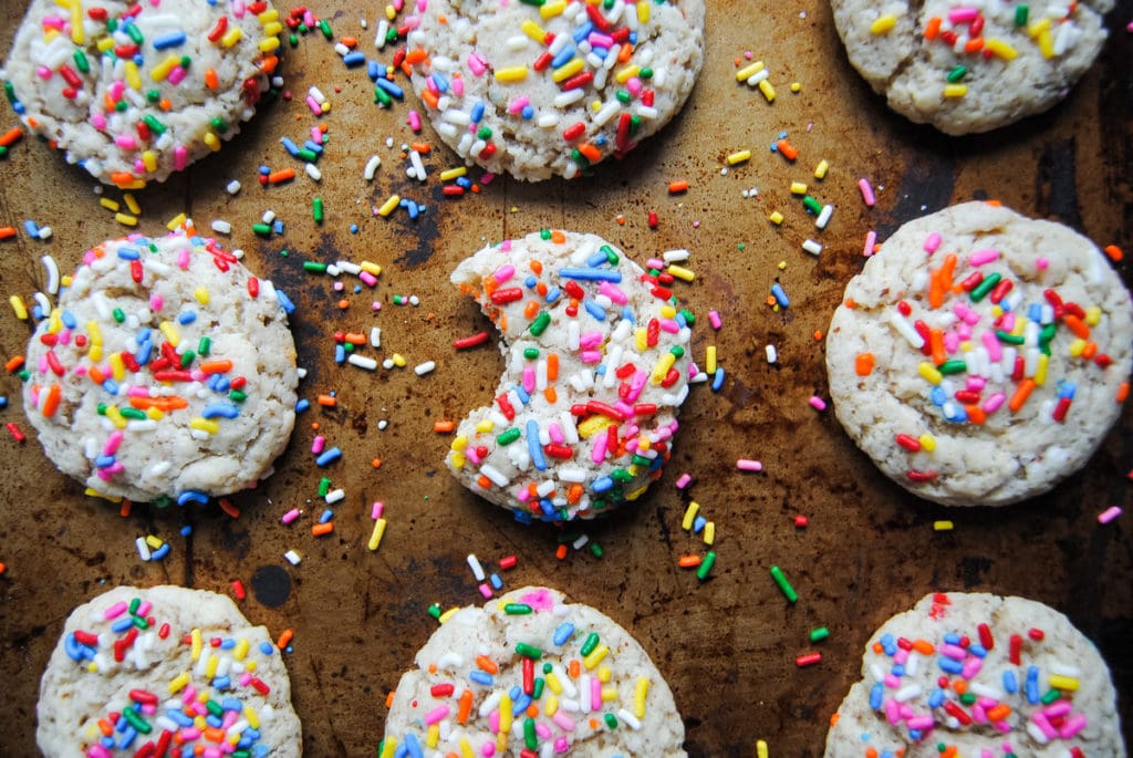 close up of sugar cookies with rainbow sprinkles on a sheet pan