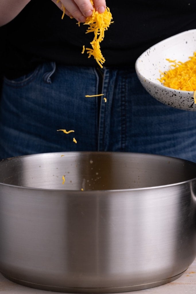 Adding freshly shredded cheddar cheese to Broccoli Cheddar Soup