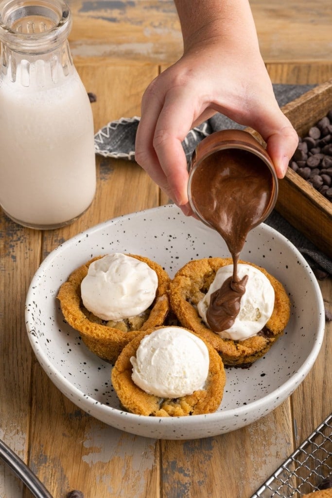 pouring chocolate sauce over cookie dough cups for ice cream