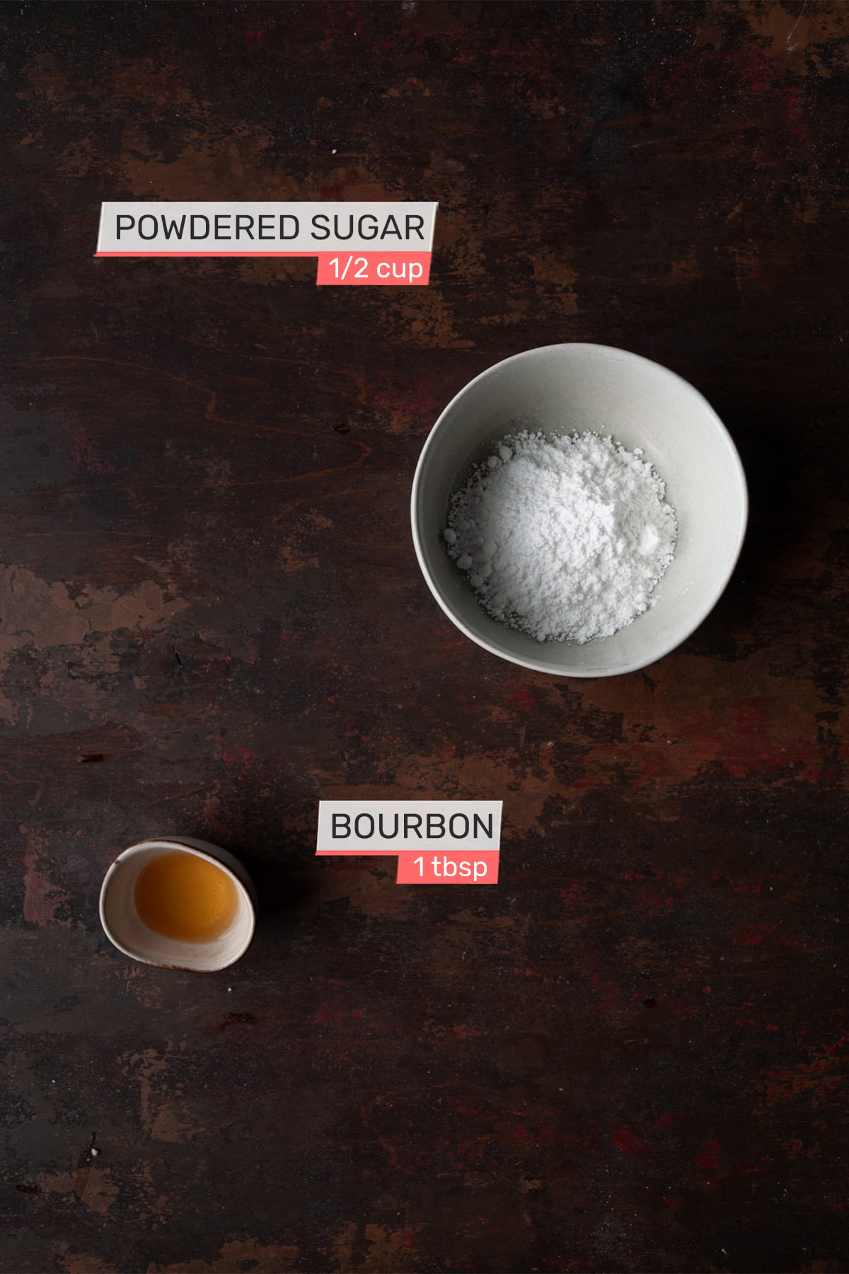 Overhead view of ingredients for bourbon drizzle on a brown wood background - powdered sugar, boubon