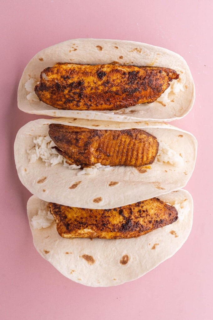 Blackened fish layered on top of coconut rice in tortilla.