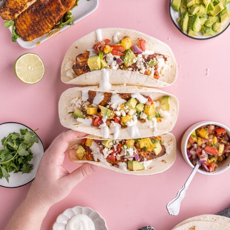 Three Fish Tacos with Pineapple Salsa with hand grabbing bottom one