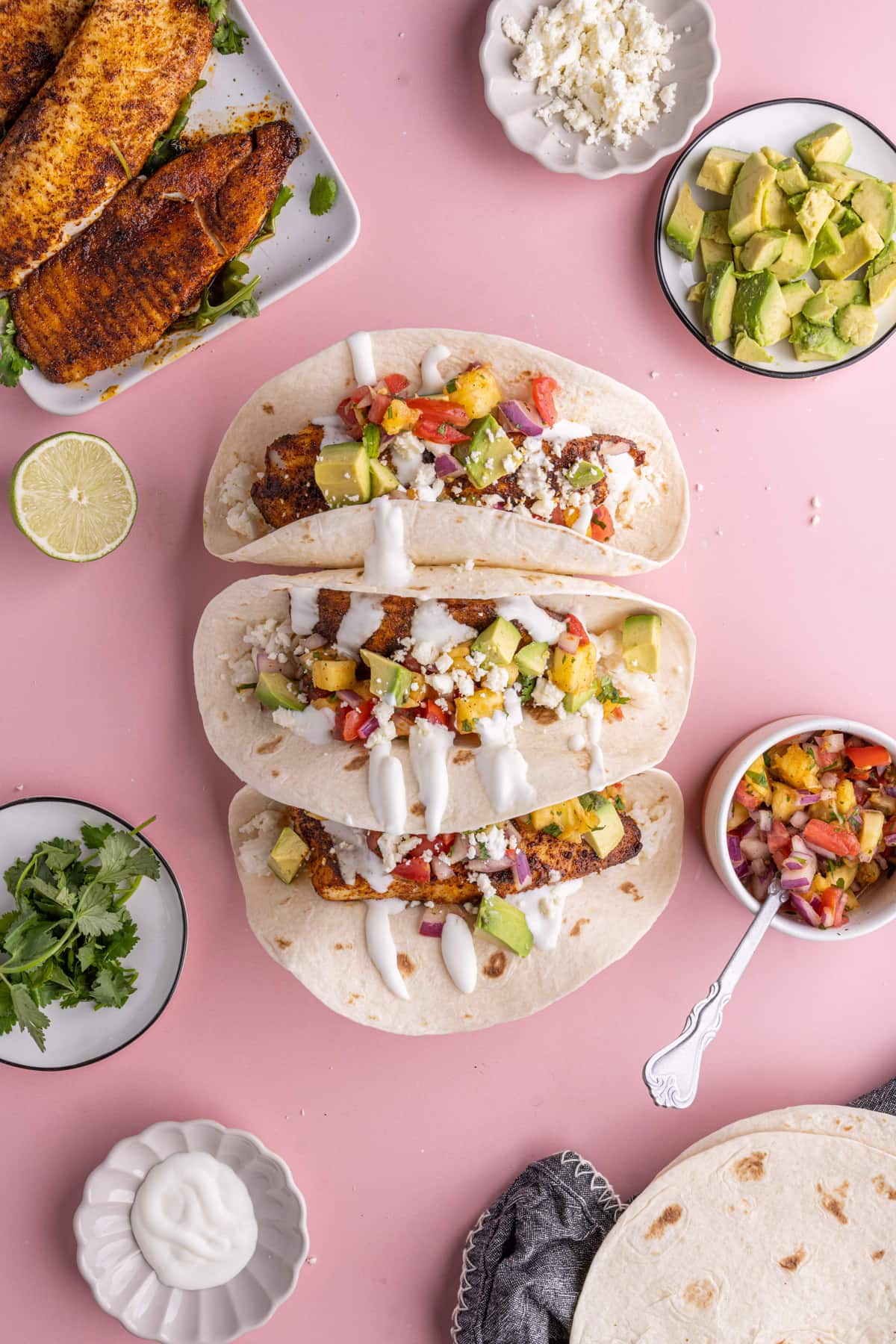 Fish Tacos with Pineapple Salsa surrounded by all the add-ins and extra fish and tortillas