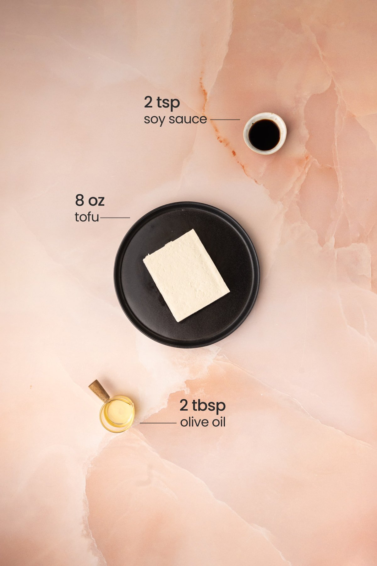 Overhead view of the ingredients needed for pan-fried tofu - soy sauce, tofu, and olive oil.