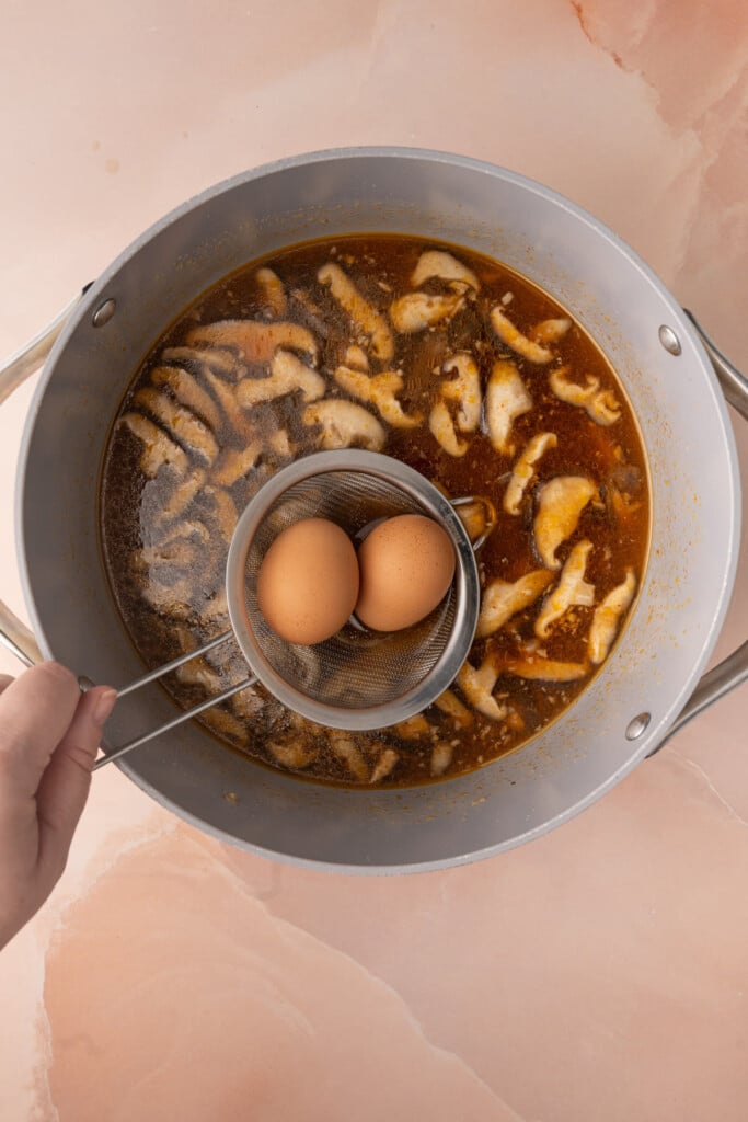 Carefully lowering clean eggs into boiling broth to soft boil them. 