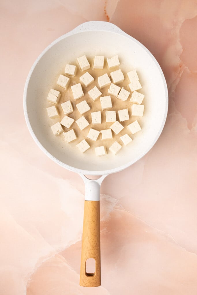 Adding pressed and cubed extra-firm tofu to a pan with hot oil to fry until crispy.