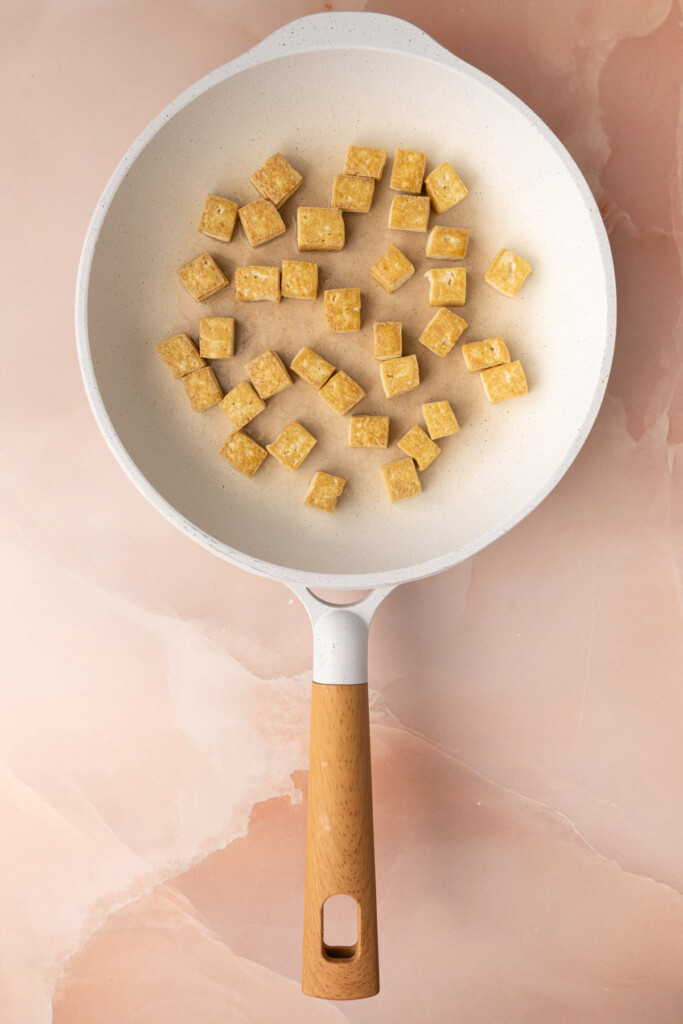Tofu pan-frying on the second side after being flipped, to reveal the crispy side of the tofu.