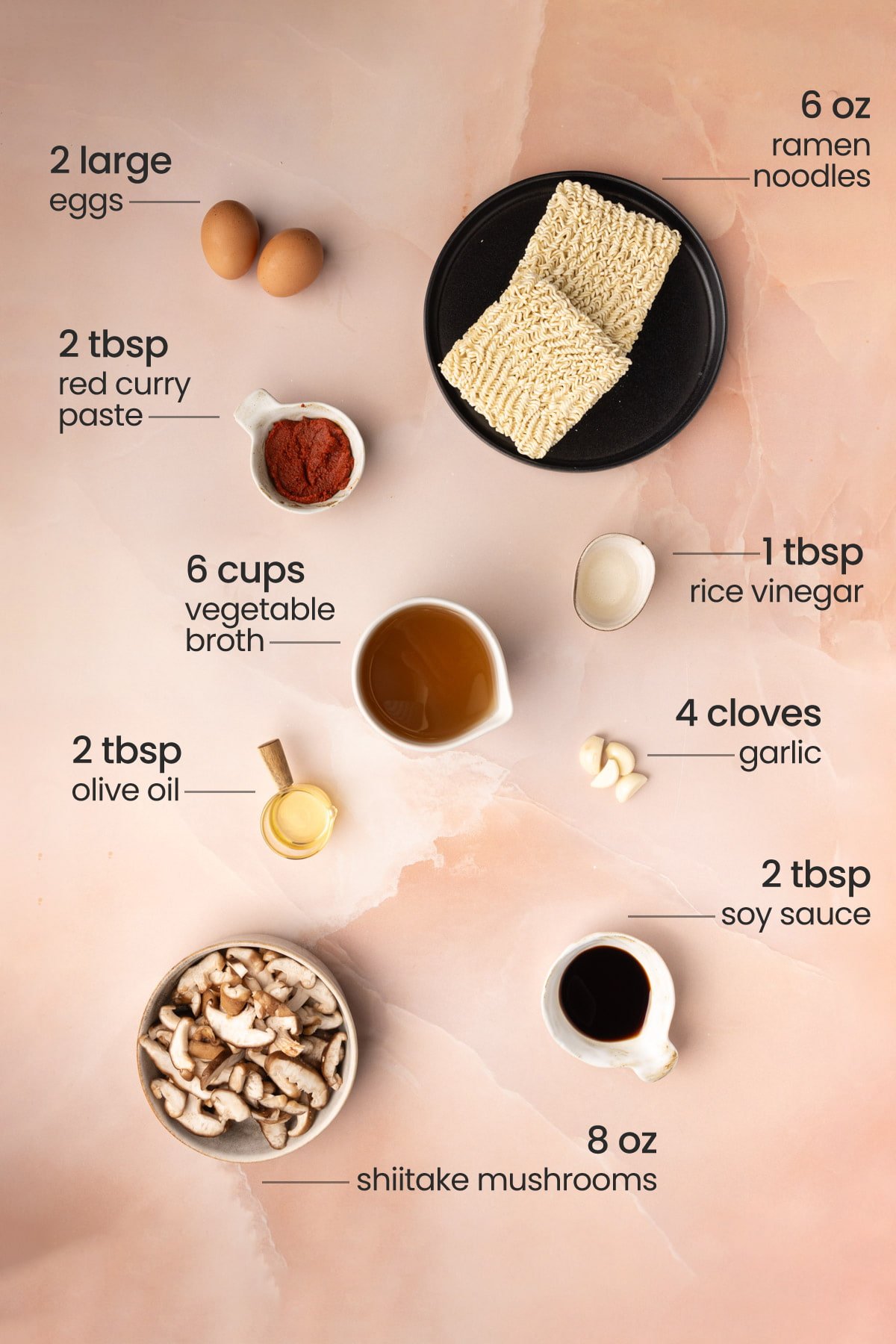 Overhead view of the ingredients needed for vegetarian ramen - eggs, red curry paste, ramen noodles, vegetable broth, rice vinegar, garlic, olive oil, soy sauce, and shiitake mushrooms