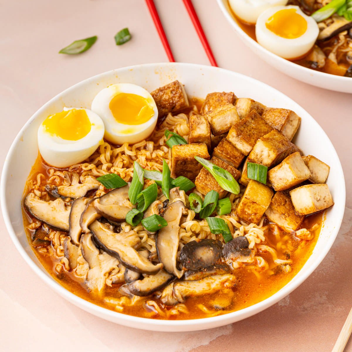 Close up of a bowl of hot ramen with tofu, soft boiled eggs., mushrooms, and green onion.