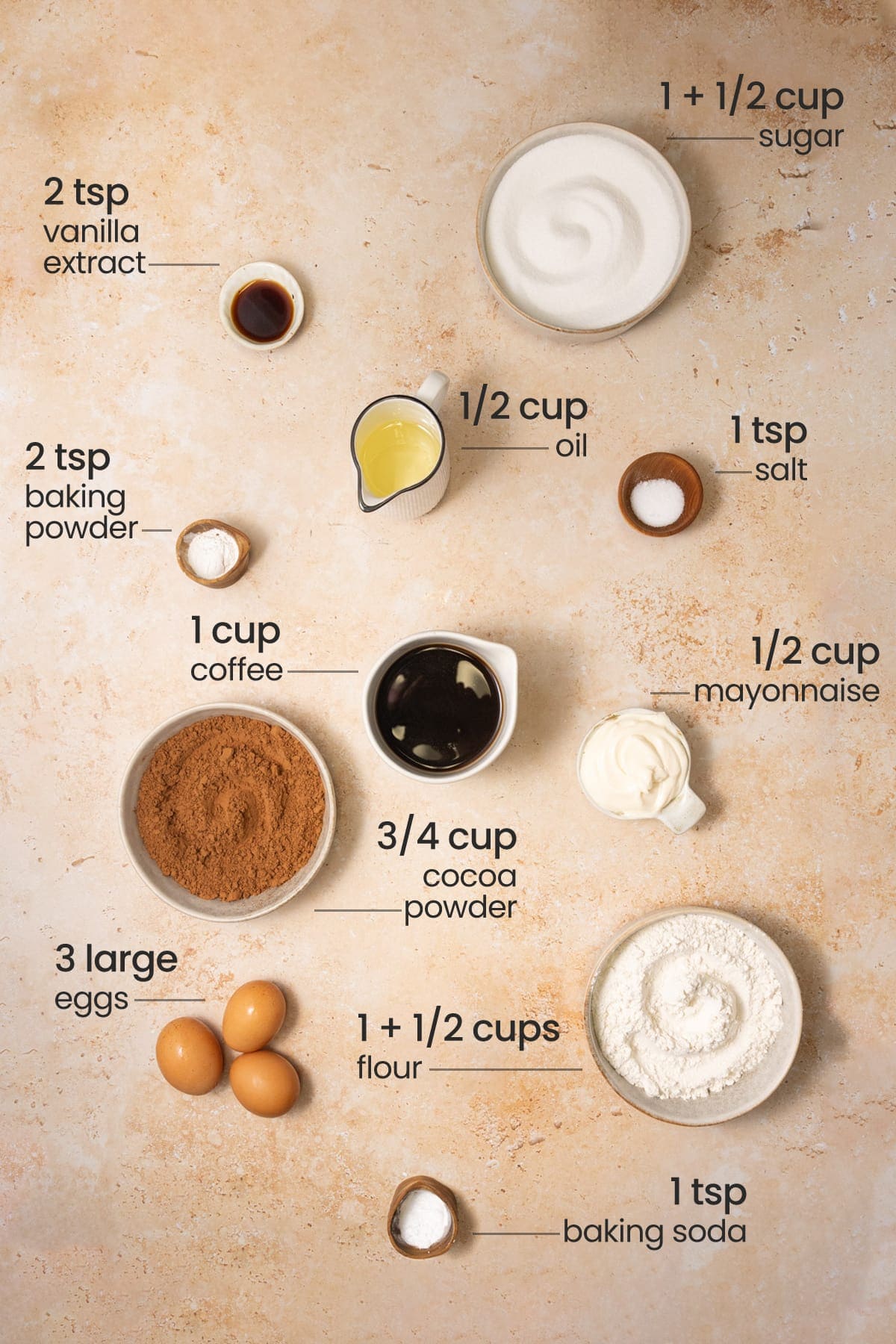 All ingredients needed for chocolate cupcakes with chocolate ganache including sugar, vanilla extract, oil, salt, mayonnaise, coffee, cocoa powder, eggs, flour, baking powder, and baking soda. 