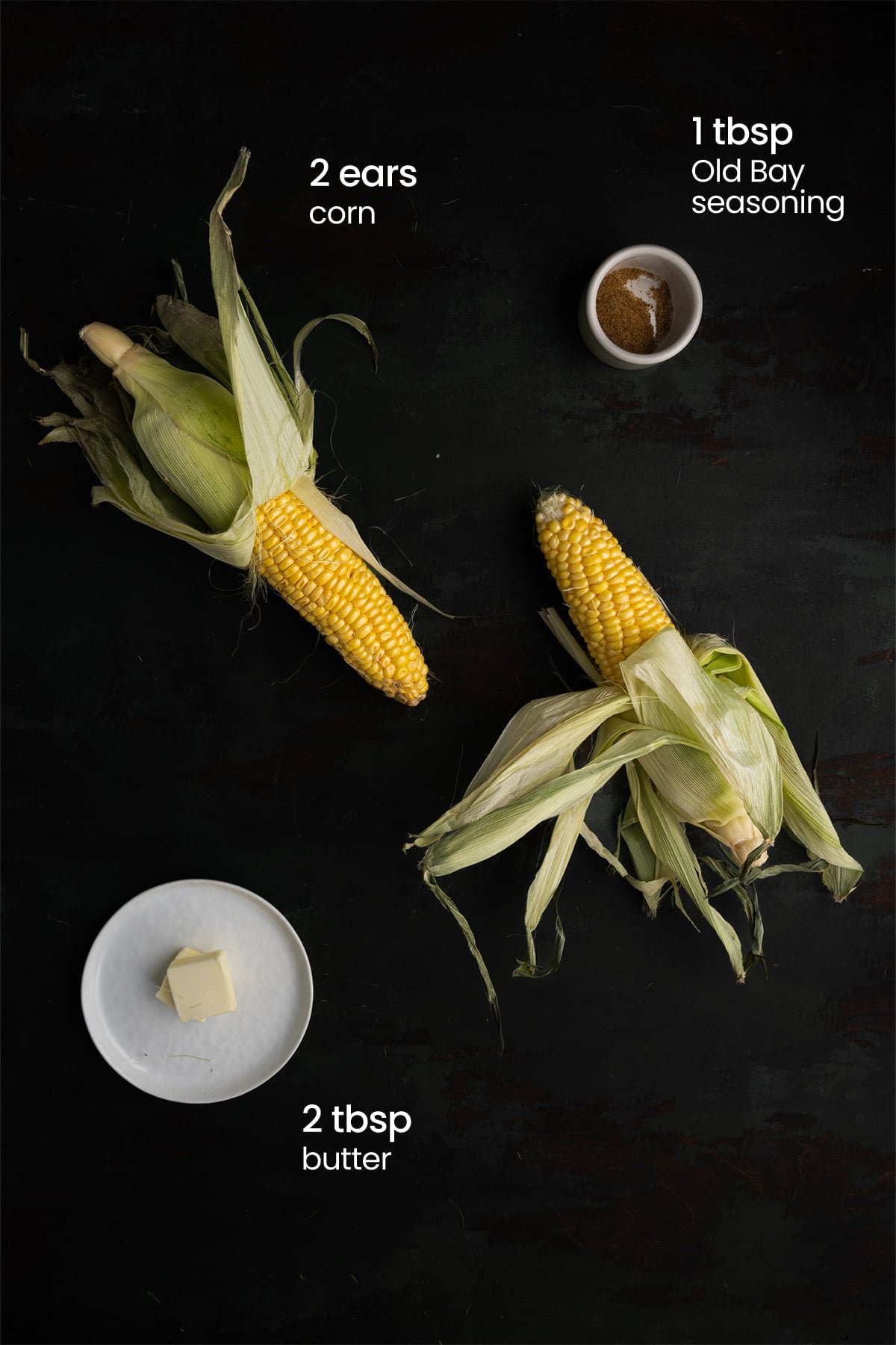 Overhead view of all the ingredients for grilled corn on the cob with Old Bay seasoning - 2 ears of corn, Old Bay seasoning, and butter.