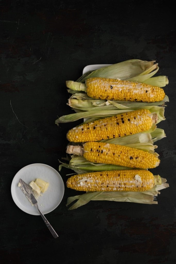 adding softened butter to grilled corn 