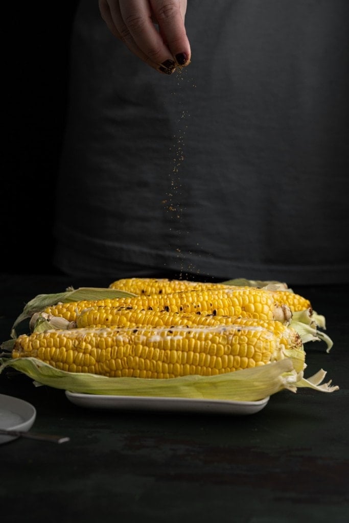 adding old bay seasoning to grilled corn